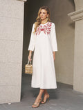 A woman stands by a stone wall in the Social Queen Butterfly Embroidered A-Line Dress, styled with gold earrings, heels, and a gold handbag—a chic choice for any wedding guest.