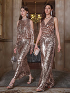 Two women walk side by side in a hallway, both wearing Social Queen’s Champagne Sequin Mermaid Skirts—floor-length, shimmering gold pieces with elegant fishtail silhouettes—paired with small clutches.