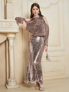 A woman stands indoors wearing the Social Queen Champagne Sequin Mermaid Skirt, featuring a floor-length, metallic finish and graceful mermaid silhouette. She pairs it with a small silver handbag.