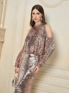 A woman wearing the Social Queen Champagne Sequin Off-Shoulder Top, holding a small purse and standing against an ornate cream-colored wall.