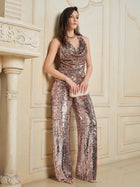 A woman stands indoors against a cream wall, wearing the Social Queen Champagne Sequin V-Neck Cami Top and holding a small clutch bag.