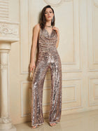 A person stands indoors in party-ready Champagne Sequin Wide-Leg Pants by Social Queen, holding a small clutch and wearing high-heeled sandals.