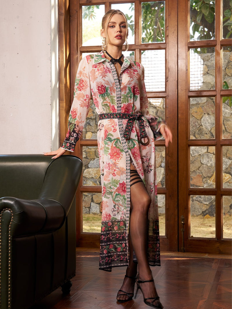 Indoors by a green sofa, a woman wears the Social Queen Color-Block Floral Embroidery Dress with sheer sleeves and black heels, standing before glass doors with a stone wall outside.