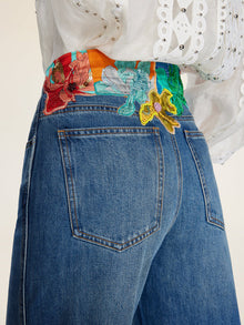 Close-up of a person wearing Social Queen Colorblock Floral Embroidery Jeans featuring high-waist, wide-leg, hand-distressed denim and floral embroidery at the waist, paired with a white eyelet blouse.