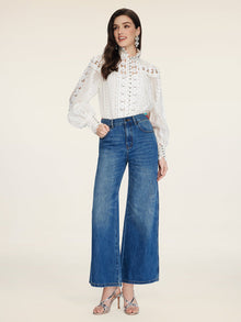 A woman in a white lace blouse, Social Queen Colorblock Floral Embroidery Jeans, and silver heeled sandals stands against a plain beige background.