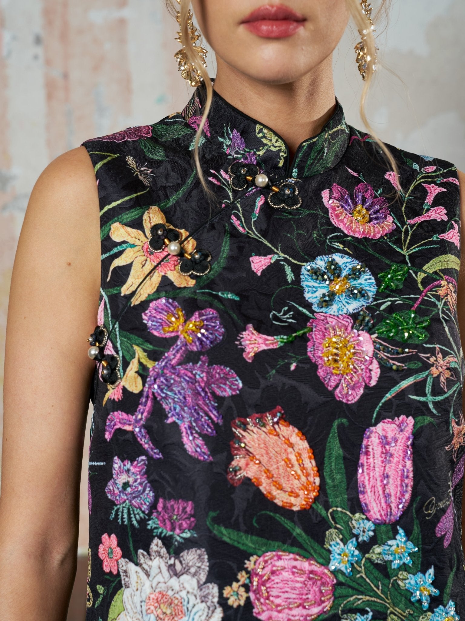 A woman wears the Social Queen Colorful Floral Mandarin Collar Dress, a sleeveless black piece featuring colorful floral embroidery, bead embellishments, and decorative buttons at the collar and shoulder.
