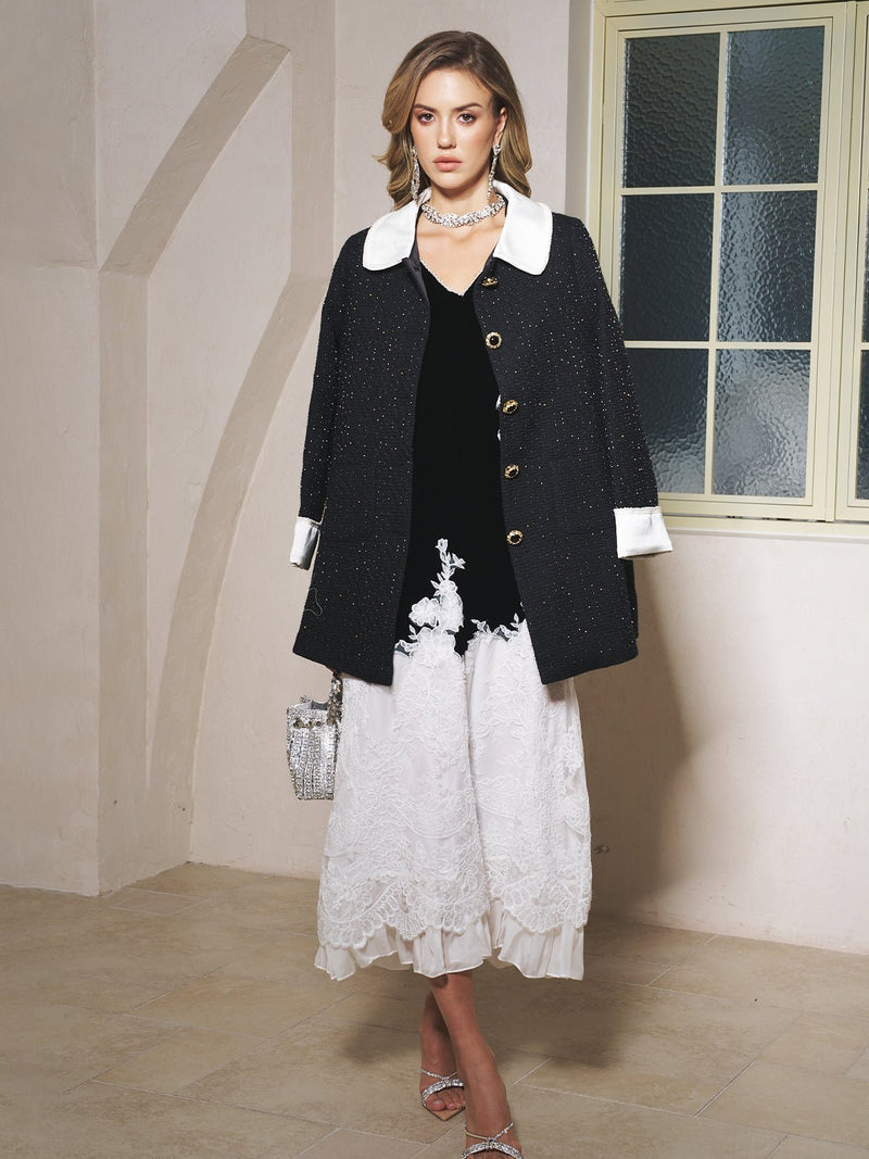 A woman stands indoors in the Social Queen Contrast Collar Tweed Coat, featuring black-and-gold tweed with white collar and cuffs, over a black top and white lace skirt, holding a small handbag for vintage elegance.