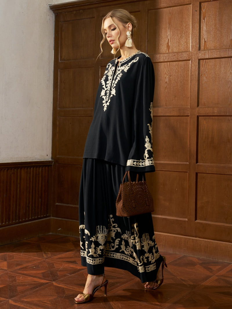 A woman stands indoors against wood-paneled walls wearing the Social Queen Contrast Embroidered A-Line Skirt, styled with a brown handbag, heeled sandals, and large earrings.