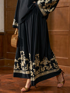 Wearing the Social Queen Contrast Embroidered A-Line Skirt, a person stands in heeled sandals with a wooden bag on a wooden floor against a wood-paneled wall.