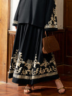 A person wearing the Social Queen Contrast Embroidered A-Line Skirt stands on a wooden floor in sandals, holding a brown cut-out purse.