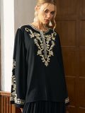 A woman stands indoors near wooden panels, wearing the Social Queen Contrast Embroidered Relaxed Blouse—a black chiffon blend long-sleeve top with intricate contrast embroidery.