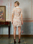 A woman stands indoors facing away, wearing the Social Queen Contrast Floral Embroidered Mini Dress and holding a small purse. To her left is a table with a framed flower painting.