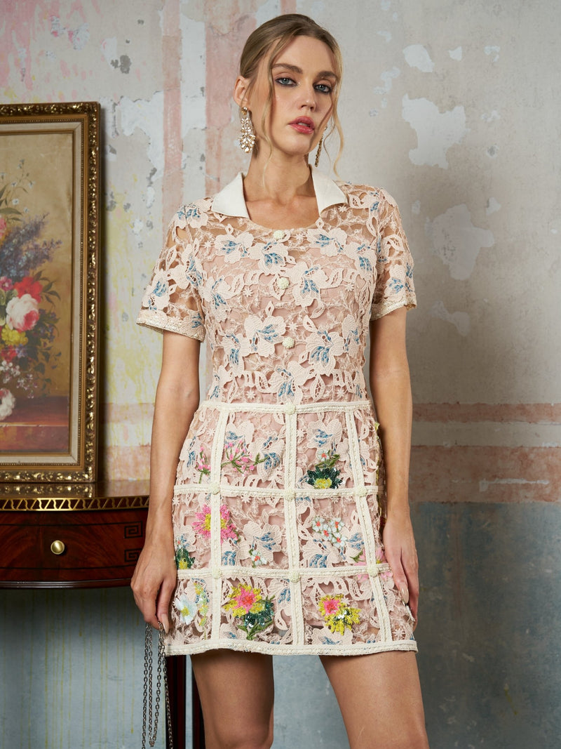 A woman indoors wears the Social Queen Contrast Floral Embroidered Mini Dress, featuring a fitted silhouette and white collar, standing by a wooden table with a framed floral painting behind her.