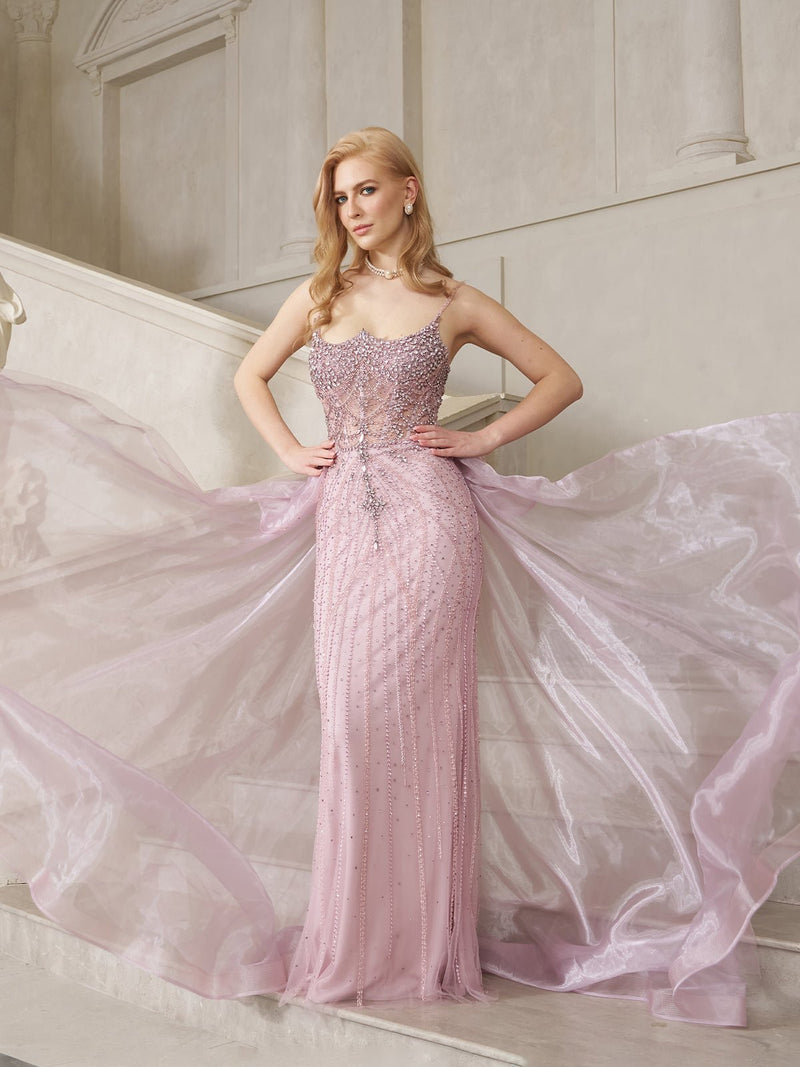 A woman poses on stairs in the Social Queen Couture Beaded Tulle Mermaid Gown, its sheer, hand-beaded tulle and fitted silhouette elegantly fanned out behind her in a luxurious interior.