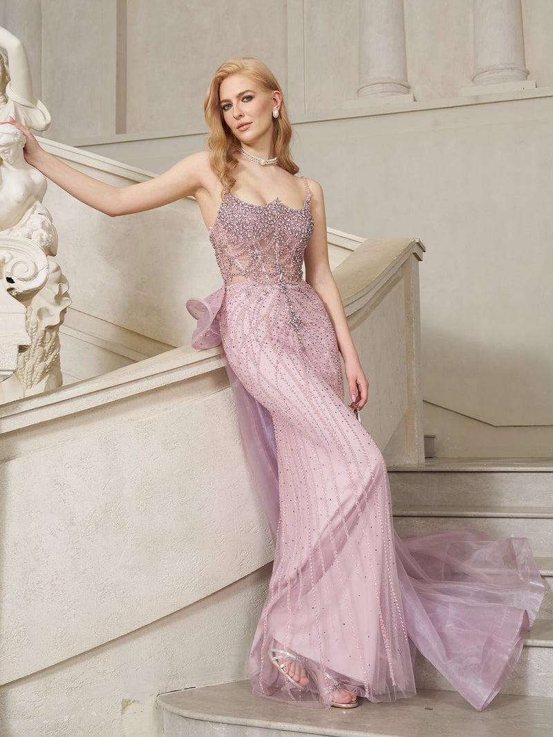 Wearing the Social Queen Couture Beaded Tulle Mermaid Gown, a woman poses gracefully on a curved staircase beside a white statue.