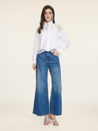 A woman faces forward in the Social Queen Cropped Embroidered Lace Panel Blouse, blue wide-leg jeans, silver heels, and drop earrings against a plain light background.