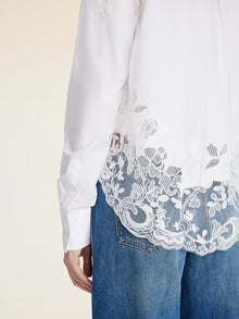 A person wearing the Social Queen Cropped Embroidered Lace Panel Blouse with blue jeans, shown from the side and back.