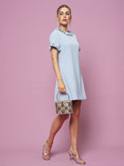 A woman in the Social Queen Crystal Beaded Trim Dress stands against a pink background, holding a small snakeskin handbag and wearing silver heels.