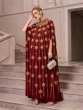 A woman stands on stairs wearing the Social Queen Crystal-Embellished Cape Dress, paired with silver sandals, statement earrings, and holding a silver clutch.