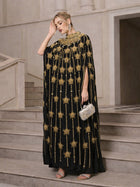 A woman stands on stairs wearing the Social Queen Crystal-Embellished Cape Dress, paired with silver heels, dangling earrings, and a silver clutch.