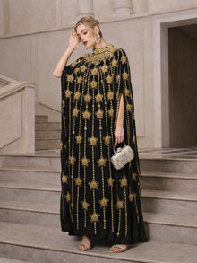 A woman stands on stairs wearing the Social Queen Crystal-Embellished Cape Dress, paired with silver heels, dangling earrings, and a silver clutch.