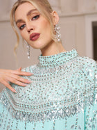 A person in Social Queen's Crystal-Embellished Cape Dress—a light blue chiffon gown with silver sequins and beads—paired with dangling crystal earrings.