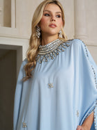 A woman stands indoors looking to the side, wearing Social Queen’s Crystal-Embellished Mock-Neck Caftan Dress paired with statement earrings.