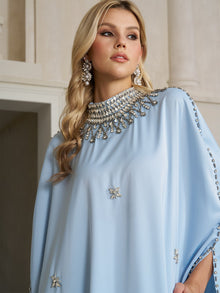 A woman stands indoors looking to the side, wearing Social Queen’s Crystal-Embellished Mock-Neck Caftan Dress paired with statement earrings.