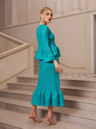 A woman in Social Queen’s Crystal-Embellished Pleated Peplum Set stands on stone steps, nude heels and statement earrings accenting the chic look. Beige walls and columns create an elegant backdrop—perfect for a standout wedding guest outfit.