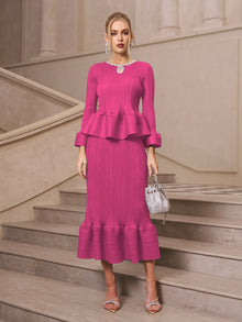 Wearing the Social Queen Crystal-Embellished Pleated Peplum Set, she stands on stone stairs with a silver handbag and strappy heels—a stylish pick for a wedding guest.