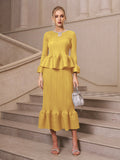 A woman wearing Social Queen’s Crystal-Embellished Pleated Peplum Set holds a silver handbag on a stone staircase, creating a chic look for a wedding guest.