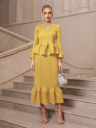 A woman wearing Social Queen’s Crystal-Embellished Pleated Peplum Set holds a silver handbag on a stone staircase, creating a chic look for a wedding guest.