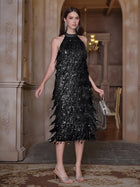 A woman stands indoors wearing the Social Queen Crystal-Embellished Sequin Fringe Halter Dress, paired with silver earrings, heels, and a small silver handbag.