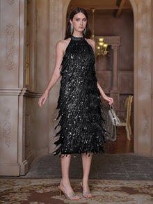 A woman stands indoors wearing the Social Queen Crystal-Embellished Sequin Fringe Halter Dress, paired with silver earrings, heels, and a small silver handbag.