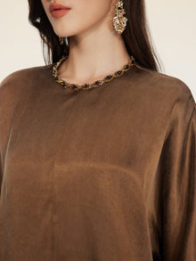 A woman shown from the shoulders up wears Social Queen's Crystal-Embellished Tencel Satin Blouse, a necklace with hand-set crystals, and a large decorative earring.