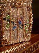 A close-up of the Social Queen Crystal-Embellished Treasure Box Bag, adorned with clear and colorful gemstones in a bird and foliage pattern and finished with a gold chain strap.