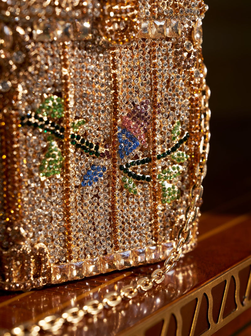 A close-up of the Social Queen Crystal-Embellished Treasure Box Bag, adorned with clear and colorful gemstones in a bird and foliage pattern and finished with a gold chain strap.