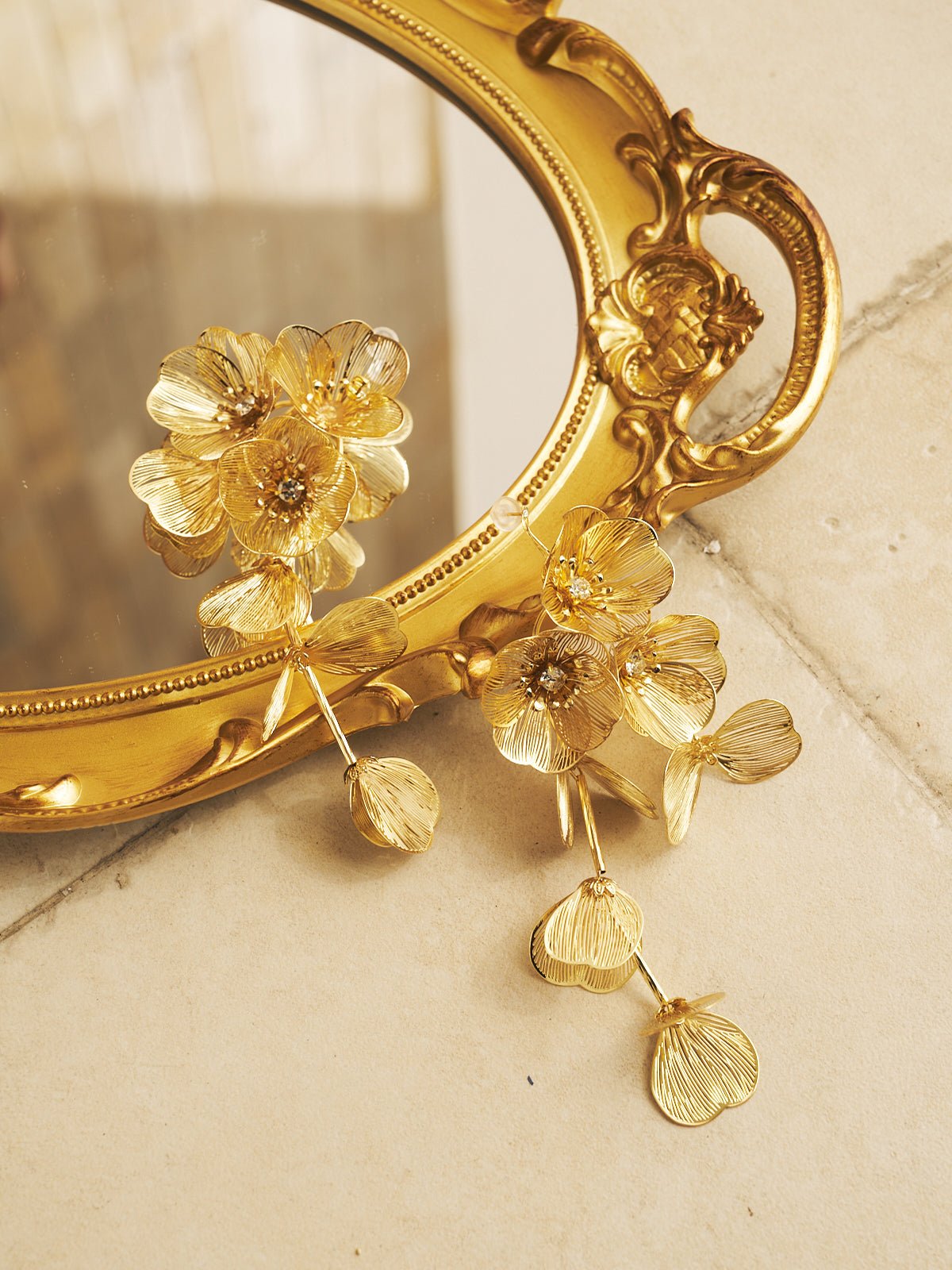 The Crystal Flower Tassel Earrings by Social Queen rest on a gold ornate mirror atop tiled flooring—an elegant accessory for wedding guests.