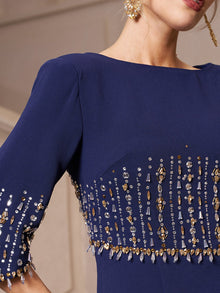 A woman wears the Social Queen Crystal Fringe Fishtail Gown, a navy blue evening dress with gold and silver beaded details and crystal embellishments on the sleeves and bodice; part of her face and an earring are visible.