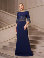 A woman in a Social Queen Crystal Fringe Fishtail Gown stands on a staircase, holding a small silver clutch.