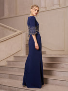 A woman in the Social Queen Crystal Fringe Fishtail Gown stands on a stone staircase, beaded fringe catching the light as she glances over her shoulder.