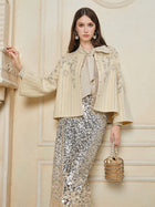 A woman wearing the Social Queen Crystal Leaf Embroidered Wool Coat, paired with a metallic sequin skirt and gold beaded handbag, stands indoors against a beige wall.