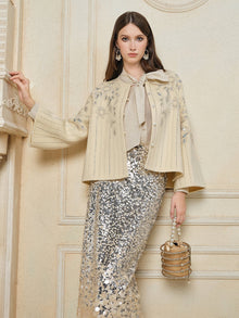 A woman wearing the Social Queen Crystal Leaf Embroidered Wool Coat, paired with a metallic sequin skirt and gold beaded handbag, stands indoors against a beige wall.