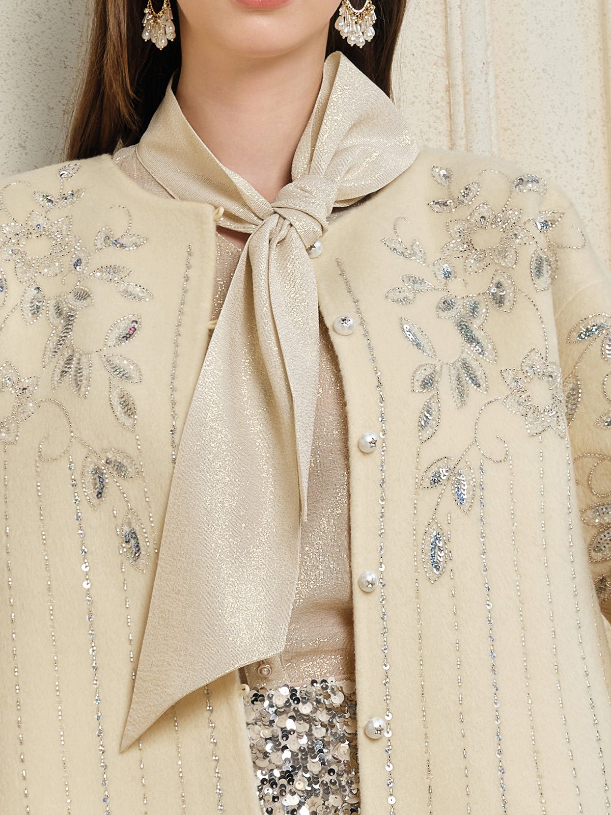 A woman wears Social Queen's Crystal Leaf Embroidered Wool Coat, styled with a shimmery neck scarf and a skirt detailed with leaf-patterned sequins.