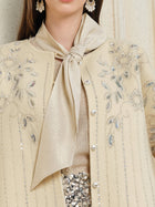 A woman wears Social Queen's Crystal Leaf Embroidered Wool Coat, styled with a shimmery neck scarf and a skirt detailed with leaf-patterned sequins.