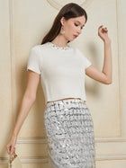 Woman posing indoors in the Social Queen Crystal & Sequin Knit Textured Crop Top, featuring diamond texture and rhinestone neckline, paired with a silver sequined fringe skirt and holding a beige handbag.