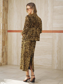 A woman in sunglasses wears the Social Queen Crystal-Trim Sequin Velvet Jacket with heeled sandals, standing indoors against a tiled wall.
