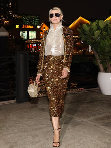 A woman in sunglasses wears the Social Queen Crystal-Trim Sequin Velvet Jacket and matching skirt, paired with a white ruffled blouse and beaded purse, as she walks outdoors at night.