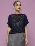 Woman poses against a pink background in the Social Queen Cutout Jacquard Knit Top, styled with a gray embroidered skirt and statement earrings.