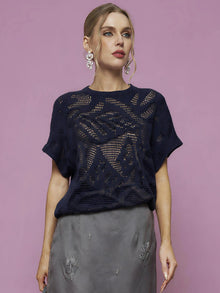 Woman poses against a pink background in the Social Queen Cutout Jacquard Knit Top, styled with a gray embroidered skirt and statement earrings.